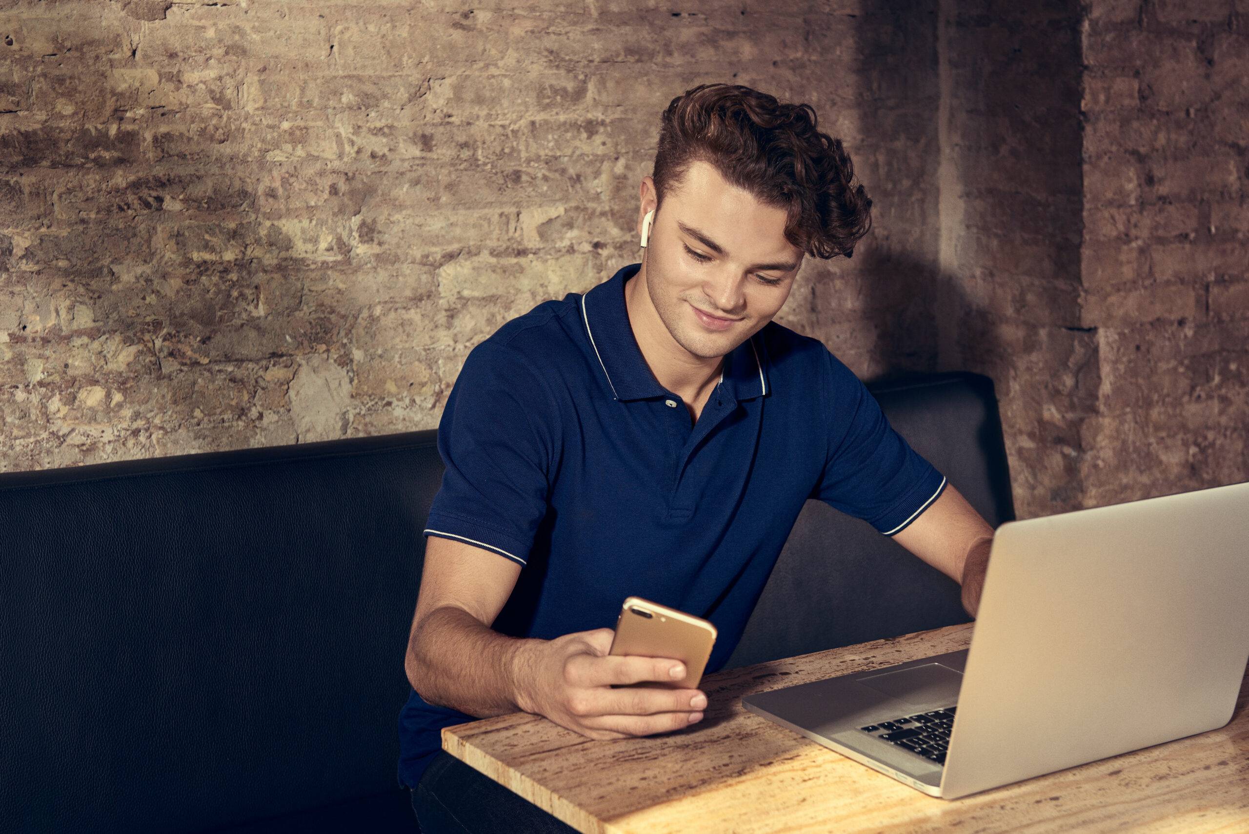 Jongen zit achter de laptop en kijkt tegelijk op telefoon