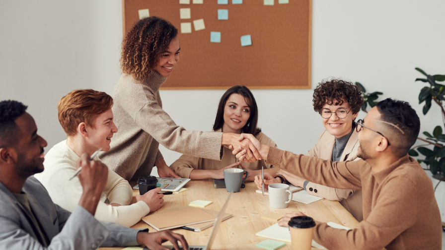 5 personen aan meeting tafel twee schudden de hand