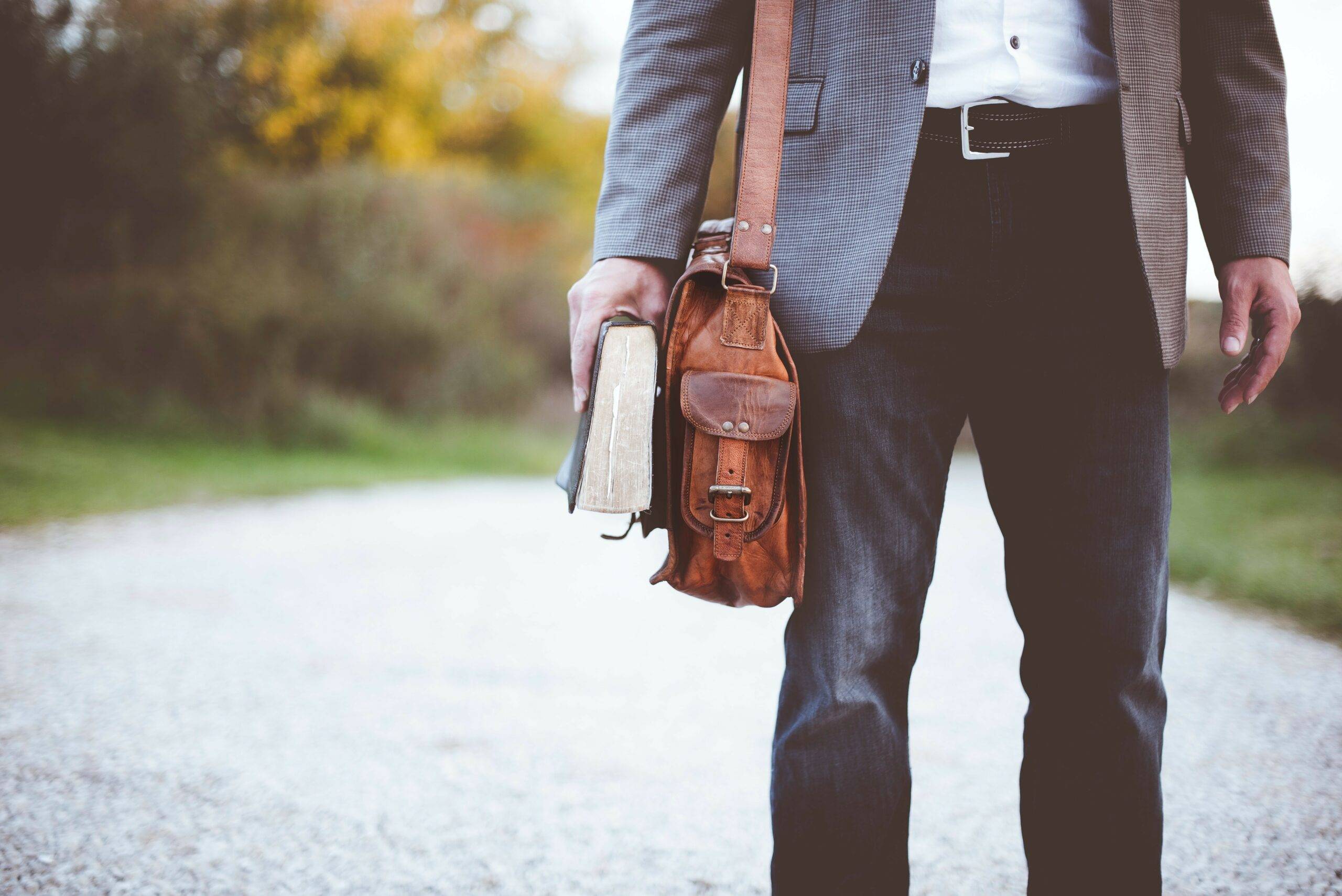 Man met boek in de hand en leren tas om