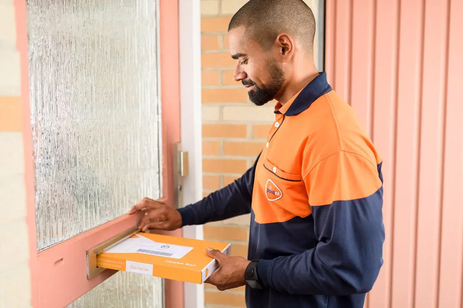 Brievenbuspakketje wordt door de brievenbus gedaan door bezorger PostNL