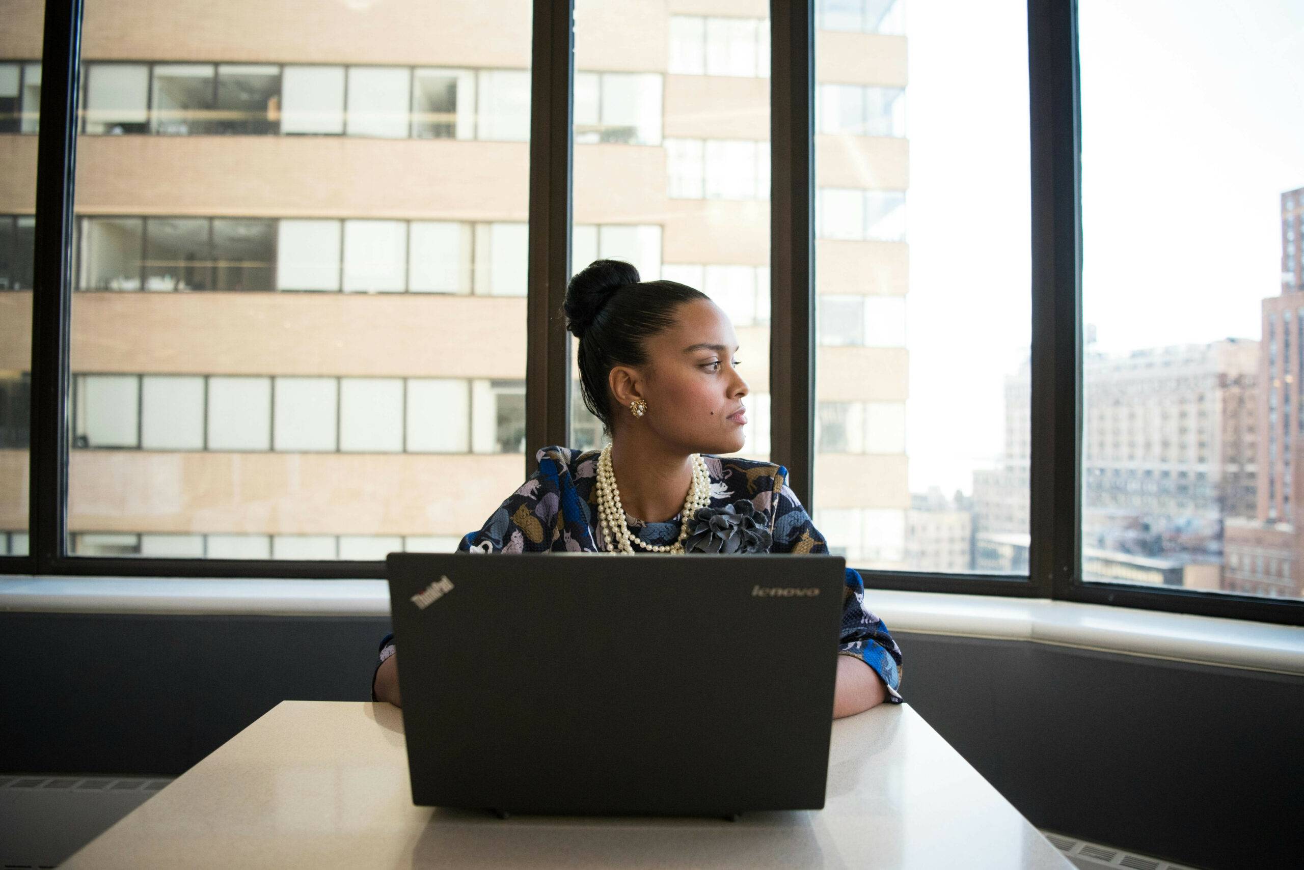 vrouw zit achter laptop en kijkt naar buiten