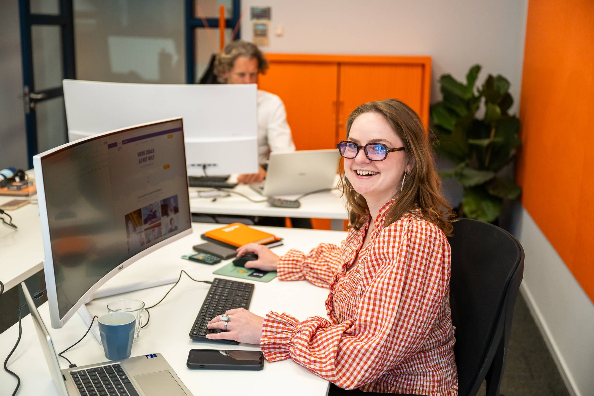 Medewerker 365Werk zit achter computer en lacht in camera