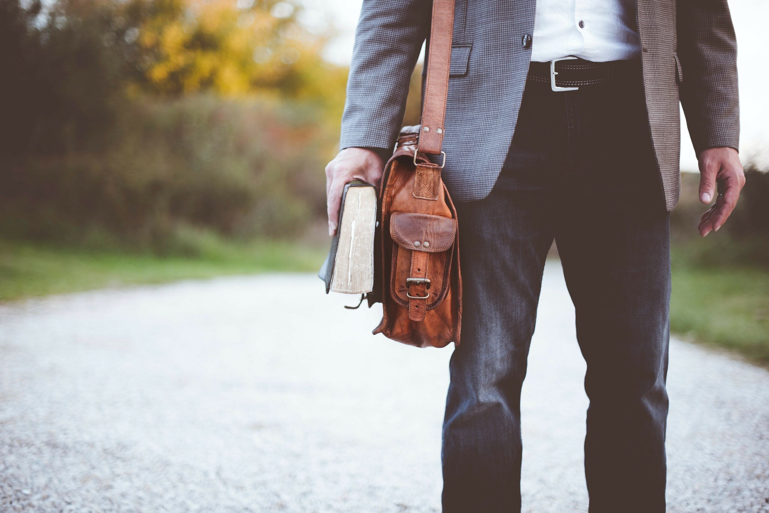 Man met boek in de hand en leren tas om